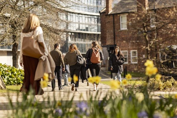 Students and staff walking on campus on a sunny spring day, with spring flowers in the foreground.