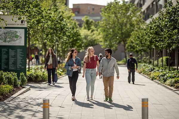 Three students walking together down a path on campus surrounded by trees.