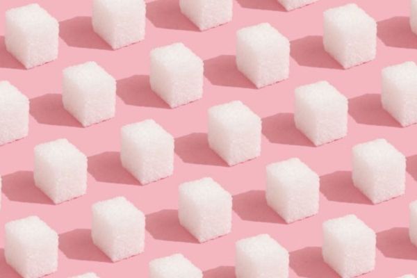 Multiple white sugar cubes lined up on a pink background.