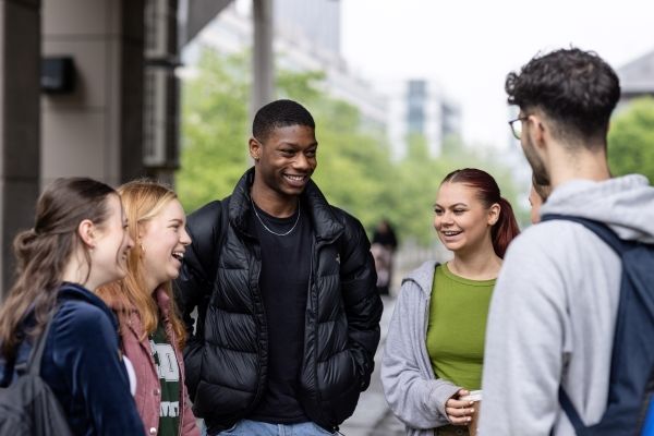 A group of five students stand outside on campus chatting and laughing.