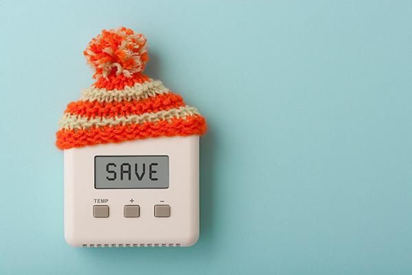 A thermostat wearing an orange and yellow bobble hat. Its screen says 'save'.