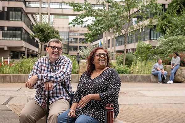 Two mature students sitting on campus laughing
