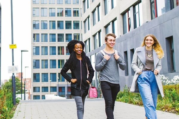 Three students chatting as they walk down a wide path next to a modern building