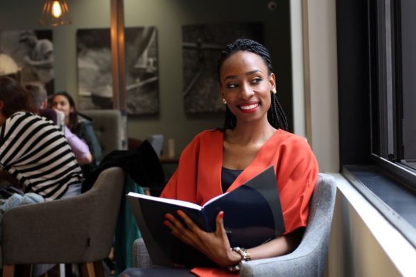 A person sitting in a cafe, holding open a large notebook and smiling.