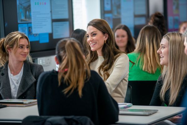 The Princess of Wales, Kate Middleton, smiling and sitting at a table with students.