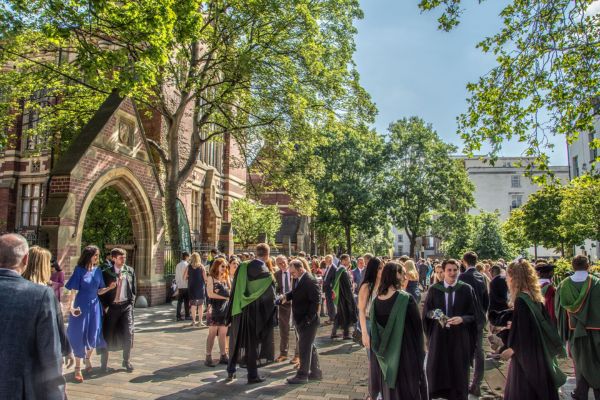 Graduates in gowns with green sashes celebrate with family outside the ivy-covered Great Hall.