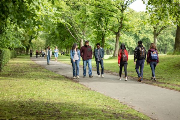 Several groups of students walk through Woodhouse Moor park in central Leeds. Trees are in full leaf.