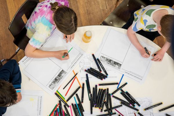 Children sat at a table drawing on sheets of paper with felt tipped pens.