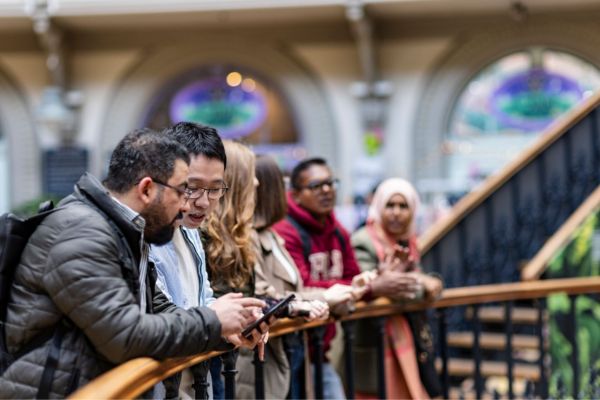 Group of students standing along ornate metal railings inside the Victorian Corn Exchange building in Leeds city centre.