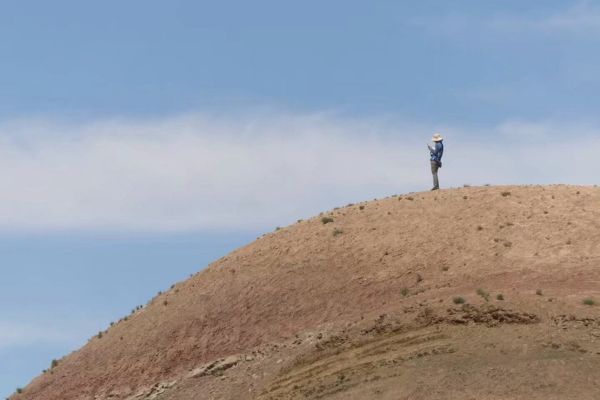 Person stands on steep brown hill against blue sky.