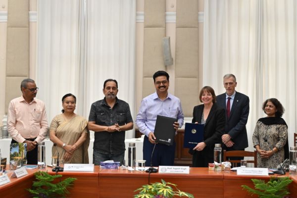 Professor Shearer West at a signing ceremony at the University of Delhi with Vice Chancellor Professor Yogesh Singh, smiling and holding agreements in leather binders.