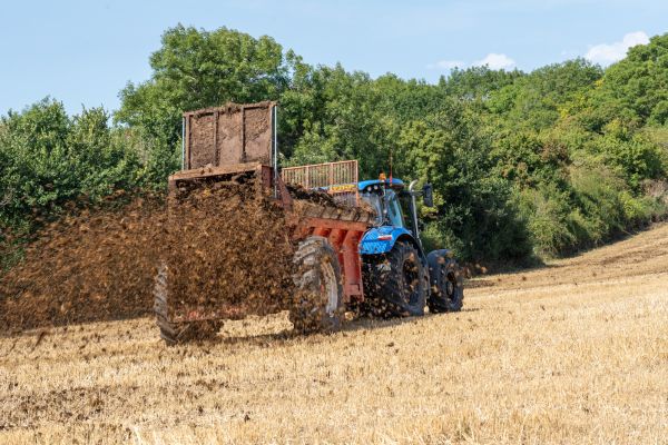 A tractor towing farm machinery in a field, spraying fertiliser onto the ground.