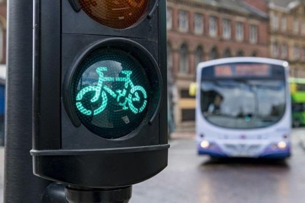 A traffic light on green for cyclists, with buses in the background.
