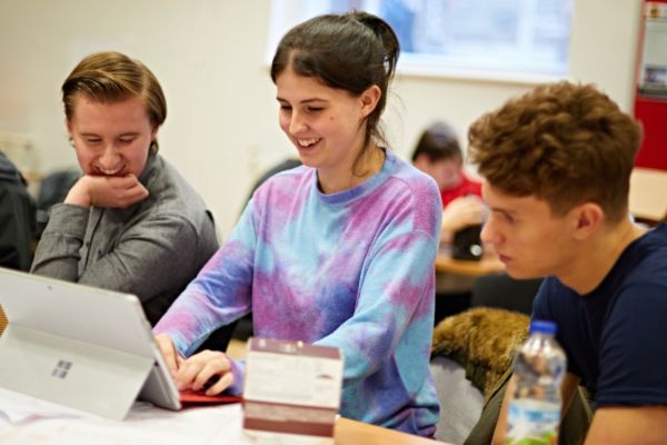 Three students on an apprenticeship programme in a classroom, studying a screen.