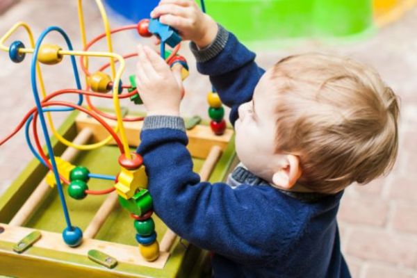 A child playing with a toy with colourful beads they can push along wooden rods.