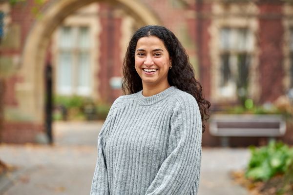 A student smiles at the camera, standing on the University of Leeds campus.