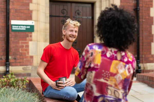 Students sat on a wall on campus chatting and smiling.