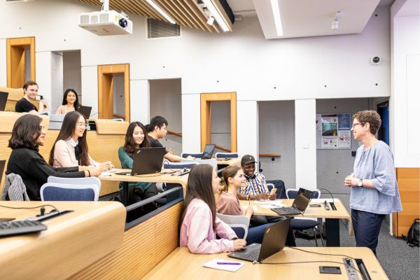 A lecturer addressing students sat in rows in a lecture theatre, working on laptops.