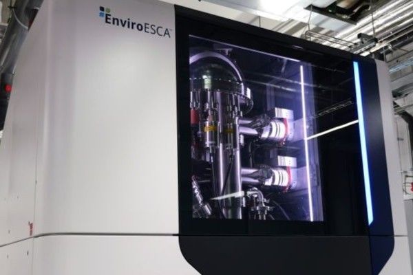 The XPS, a room-height white and black metal structure with glass door panel, featuring the EnviroESCA logo. The instrument’s wiring and mechanics can be seen through the glass panel.