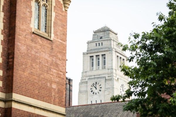 The white stone Parkinson tower, with part of a red-brick building and a tree in the foreground.