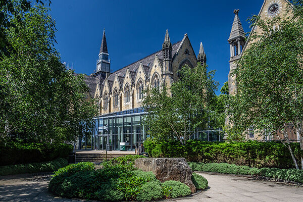 The business school entrance with a student walking out of the building, with a blue sky and leaves on the trees.