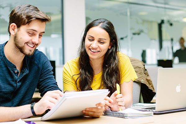 Two students reading from paper documents and smiling.