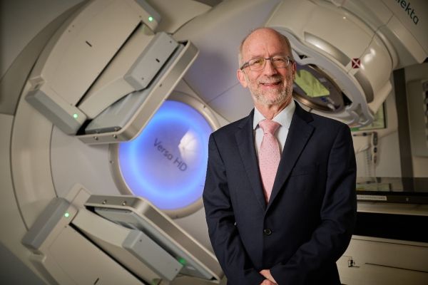 Professor David Sebag-Montefiorie smiles in front of a radiotherapy machine