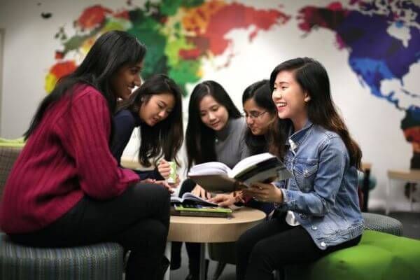 A group of students having a collaborative study session, smiling and discussing while sitting around a small table with open books.