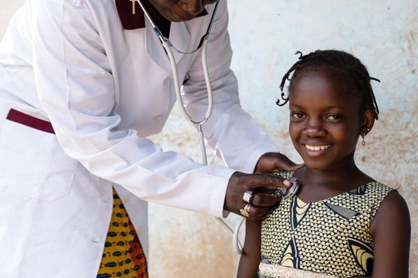 A health professional holding a stethoscope on a smiling child.