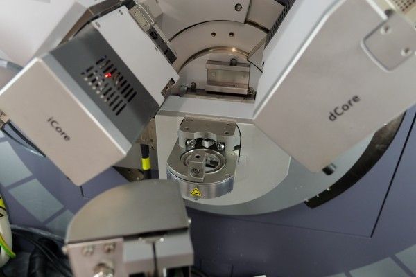 The microscope, a room-height metal and glass structure stands with its door open, revealing wiring and mechanics. The structure is branded with the FEI logo.