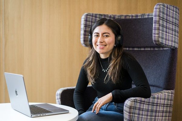 A smiling student sat in a large comfy booth with a laptop open on a table in front of them.