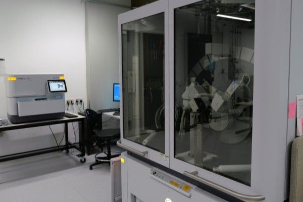 Exterior view of the diffractometer, a large white cabinet with two closed glass doors, alongside a smaller white Multicore Diffractometer, a rectangular white metal piece of equipment with a control panel screen, on top of a waist-height table.