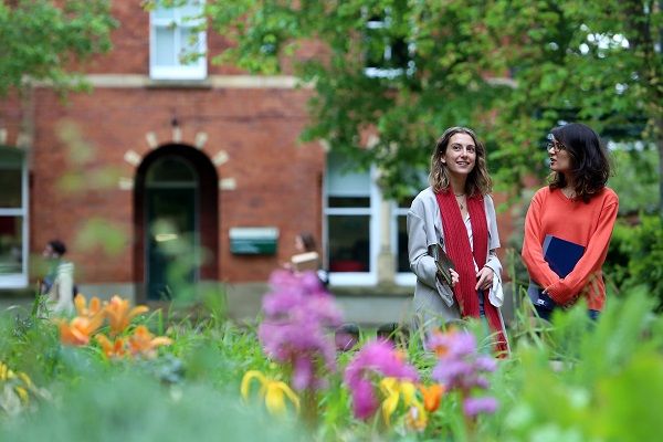 Two students chatting on campus, stood among flowers and plants.