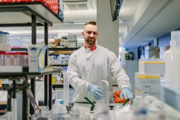 A researcher wearing a lab coat and protective gloves working in a lab.