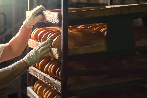 A baker handling shelves of fresh bread