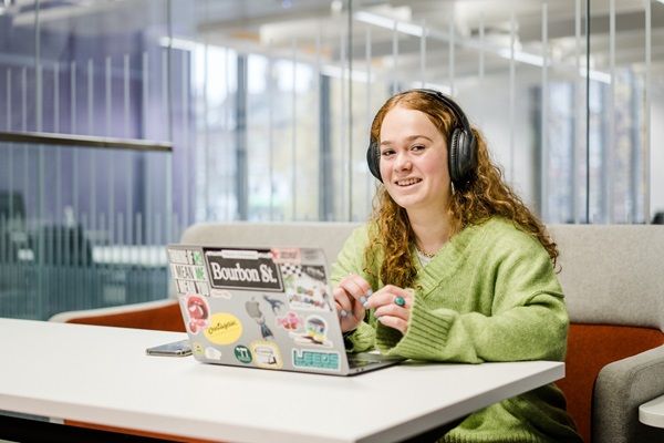 A student sat in a modern study space wearing headphones and using a laptop