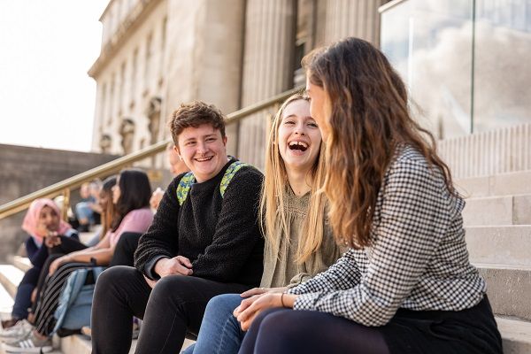 A group of students sitting on the steps in front of the Parkinson Building, chatting and laughing