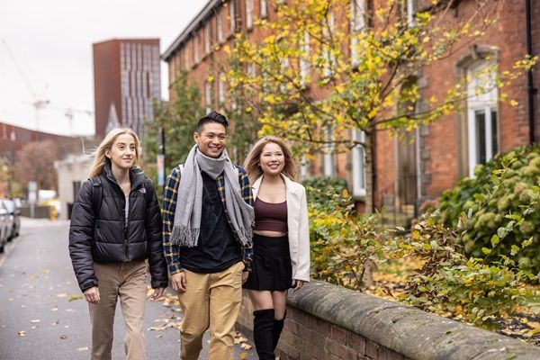 Three students walking on campus on an autumn day. In the background are red-brick houses which are student accommodation.