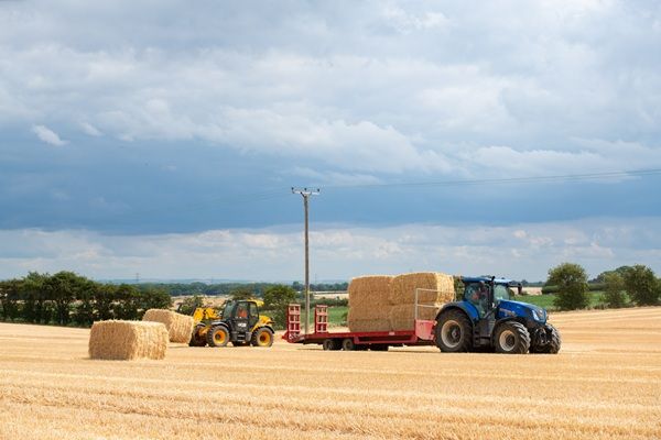 Two tractors moving large hay bales in a field