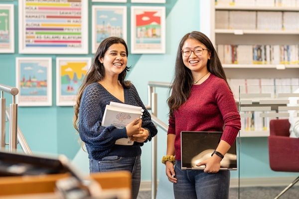 Two smiling students stood in a study space with books and posters in the background.