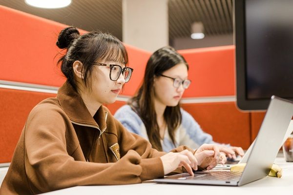 Two students working on laptops in a study booth