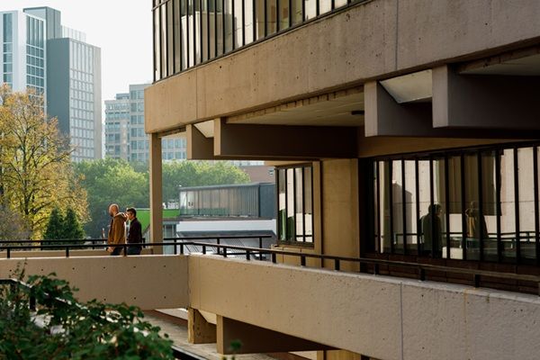 Two people walking on an elevated walkway attached to a large concrete University building.