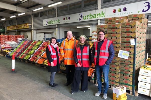 A group of researchers wearing hi-vis jackets in front of shelves of fruit and veg in a wholesalers
