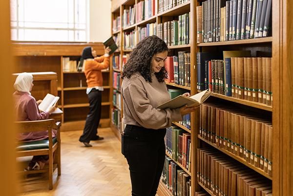 Student standing reading a book in a library