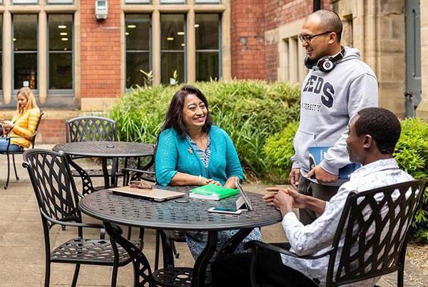 Three postgraduate researchers chat in courtyard cafe on campus