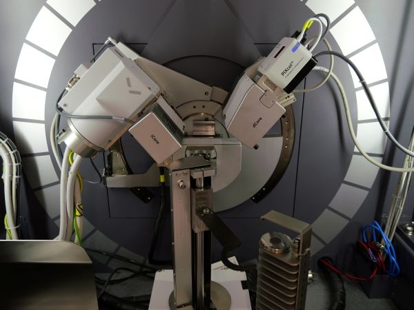 Close-up interior view of the diffractometer, showing multiple white detector and optical modules mounted at angles around a circular goniometer, with visible cables, mechanical arms, and precision stages inside a grey enclosed chamber.