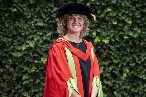 Ellie Kildunne stands smiling at the camera in red and green graduation robes and a black cap.