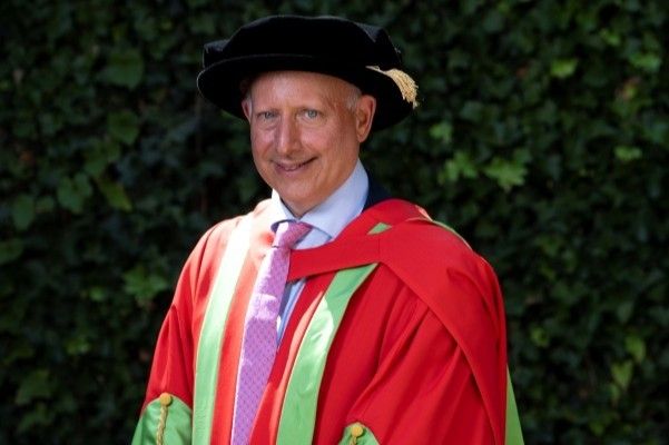 Steve Rosenberg stands smiling at the camera wearing red and green robes and a black cap.
