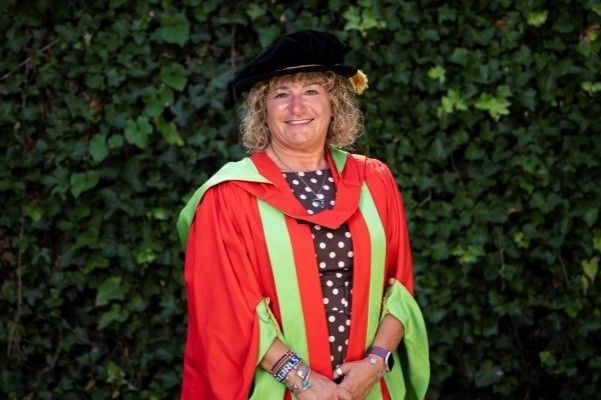 Tina Leslie stands smiling at the camera in red and green graduation gowns and a black cap.