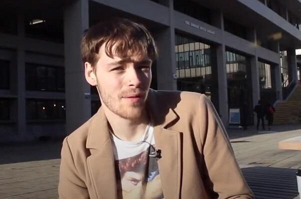 University of Leeds alumnus, George Hobley, sat on campus wearing a brown jacket.